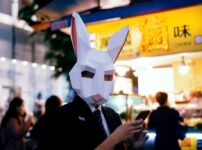 man in black jacket holding white paper mask