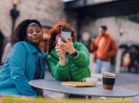 a couple of women sitting at a table with a drink and a cell phone